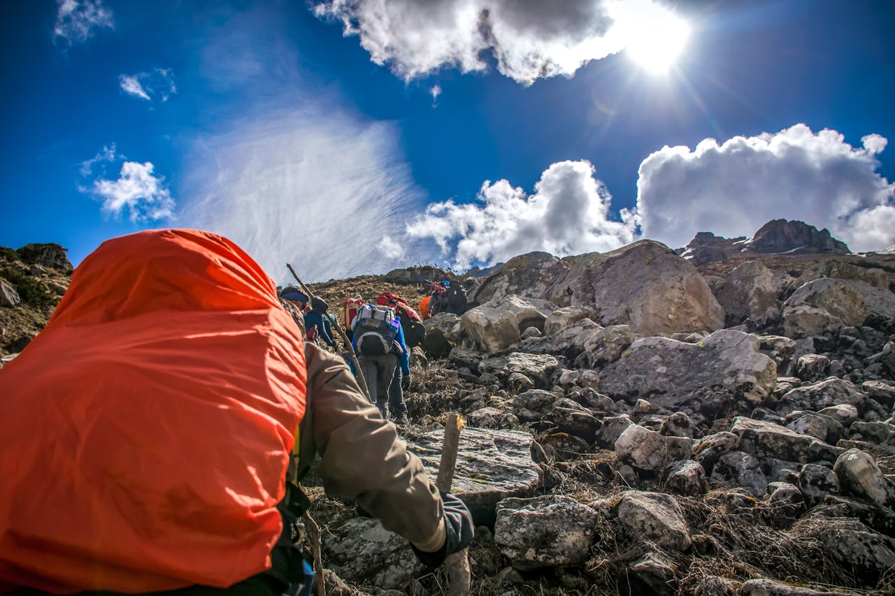 Hikers ascending a rocky mountain trail under a bright sunlit sky.