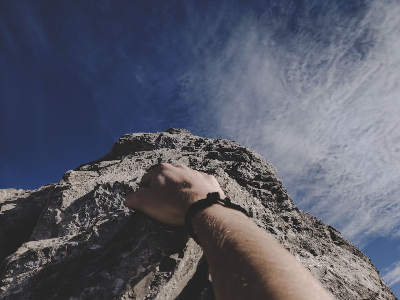 A climber's hand gripping a rocky cliff under a clear blue sky, embodying adventure.
